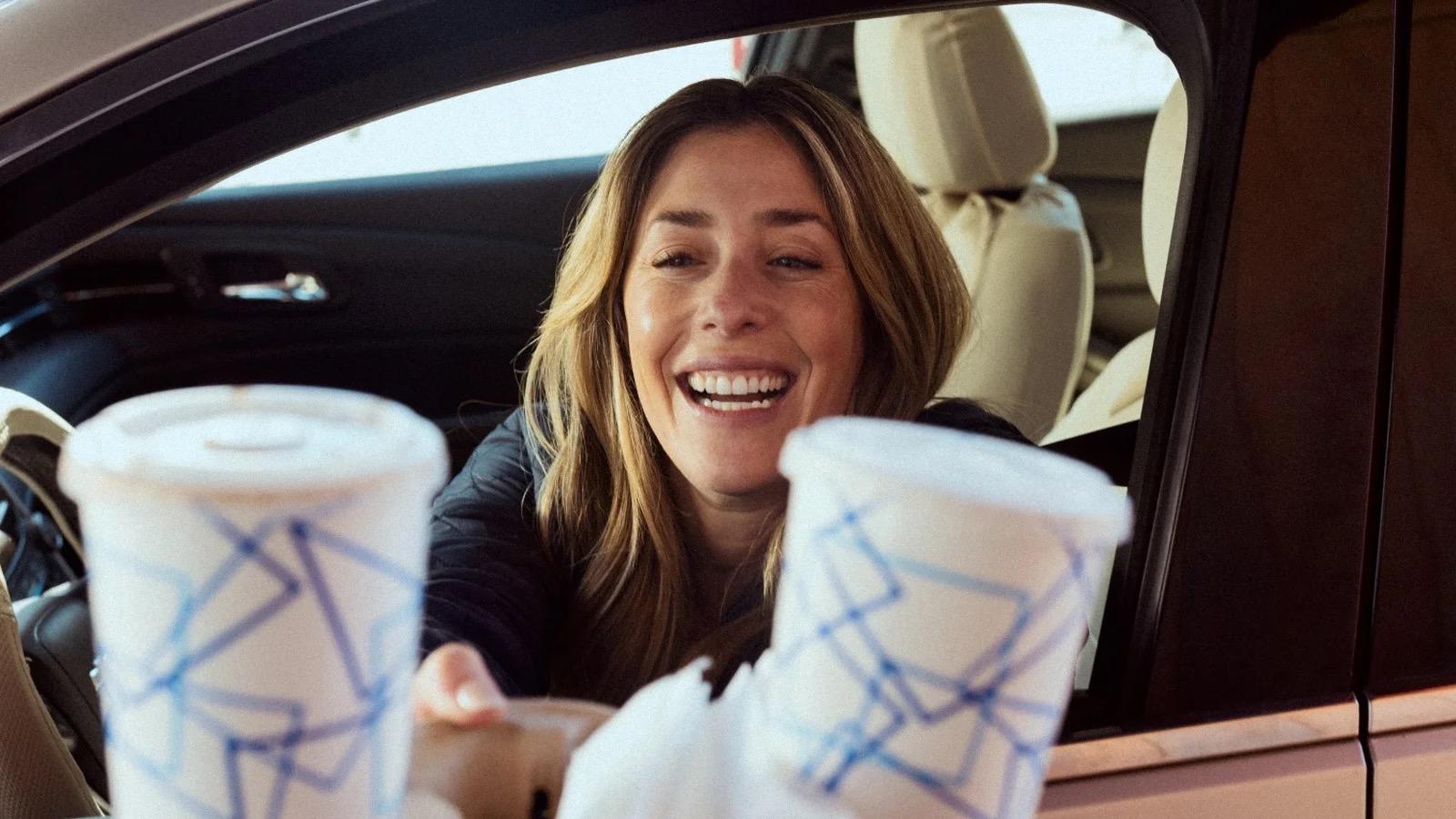 Smiling customer reaching for drinks at a drive-thru window