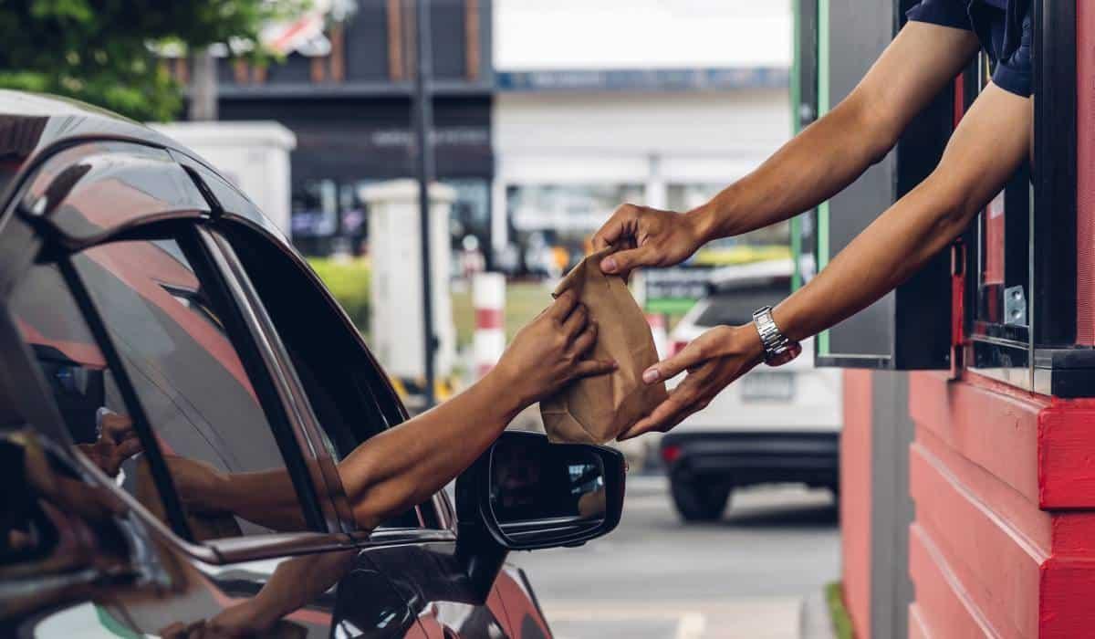 Drive-thru employee handing a paper bag to a customer in a car