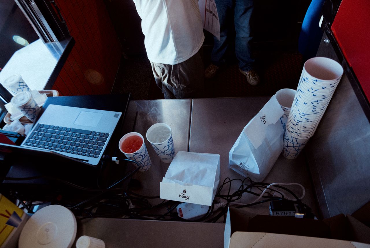 Workspace with laptop, coffee cups, and takeout bags on a table.