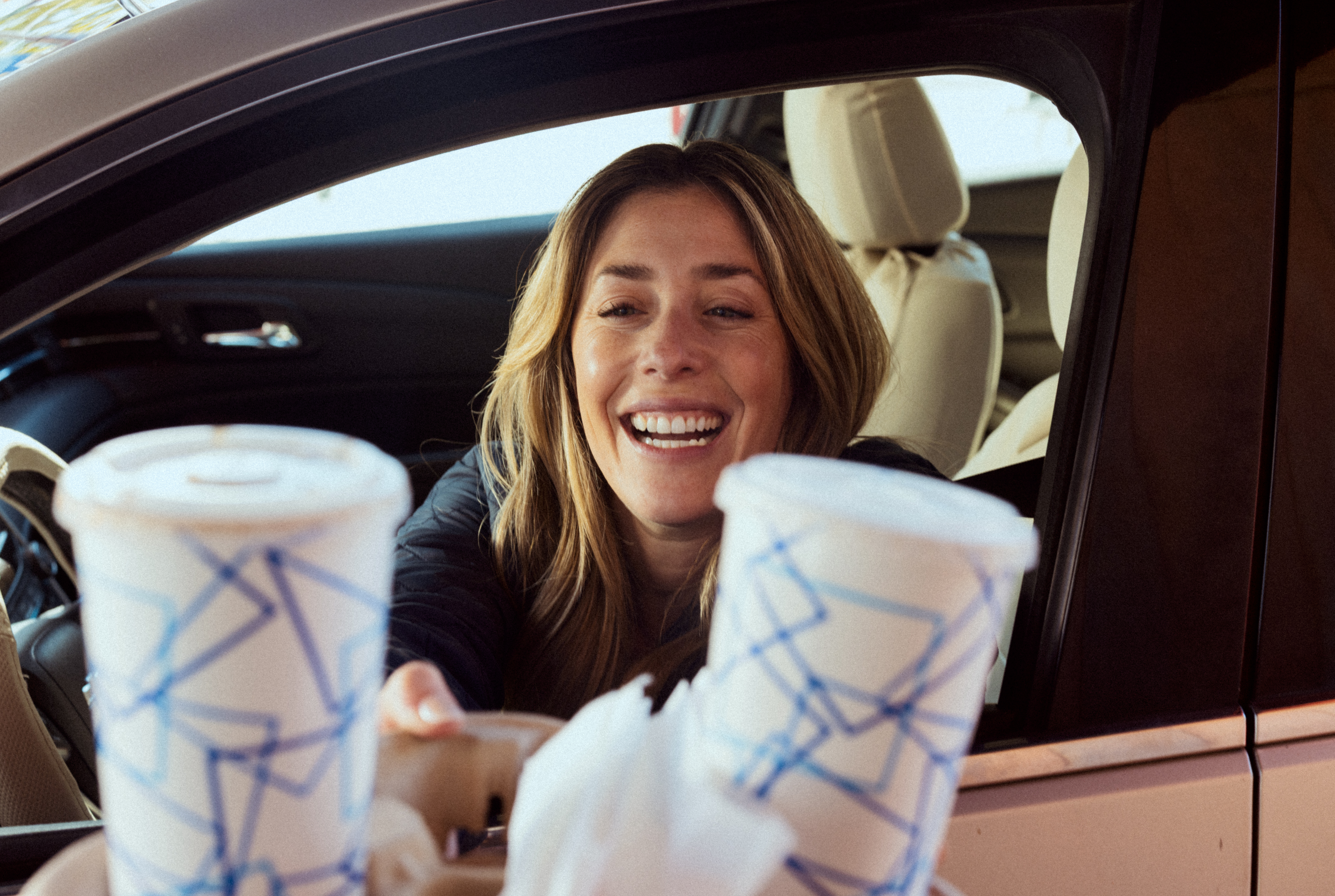 Smiling customer in her car receiving a coffee from the drive-thru window.